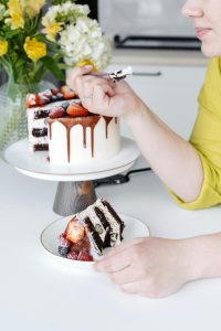 A woman enjoys a slice of delicious chocolate drip cake adorned with fresh strawberries and blueberries.