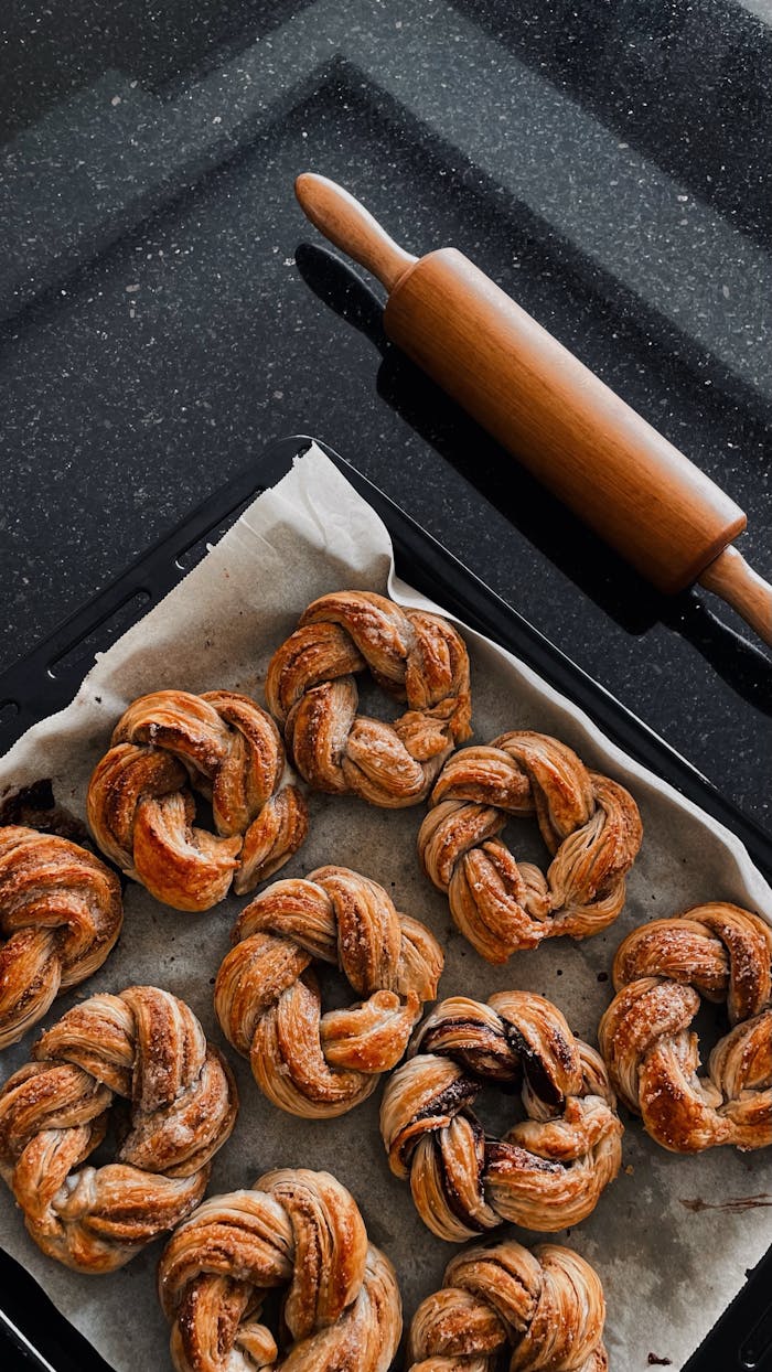 our-services-3 Delicious homemade twisted buns on a baking tray with a rolling pin nearby. Perfect for bakery lovers.